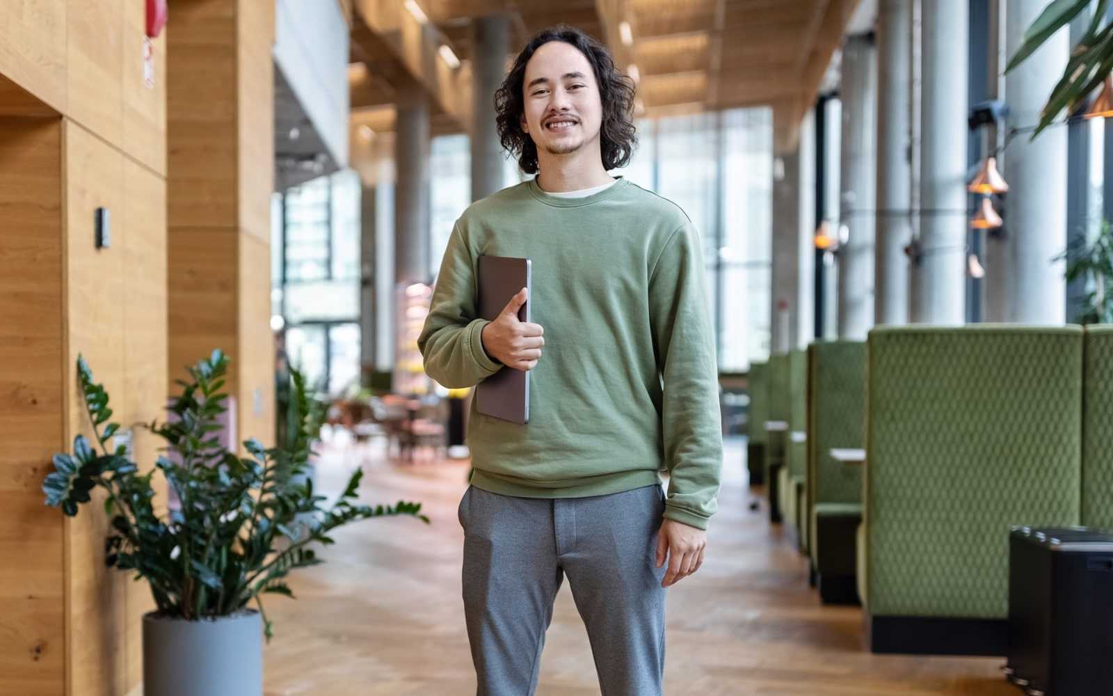 employee stands in a modern office lobby holding a laptop